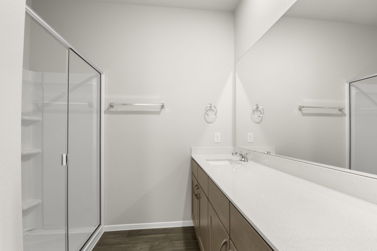 Image of a bathroom with brown wood-like flooring and white vanity with mirror and a walk-in shower