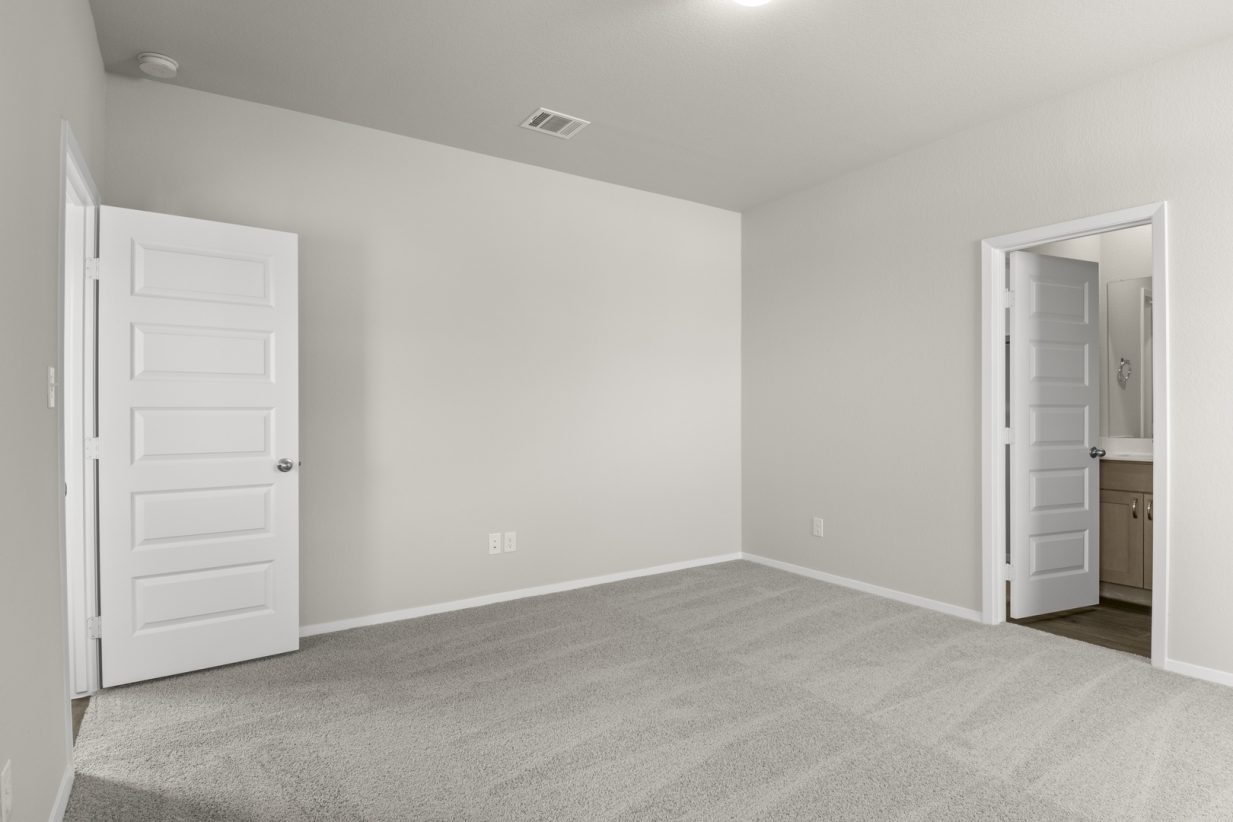 Image of primary bedroom with tan carpet and light grey walls and a white door