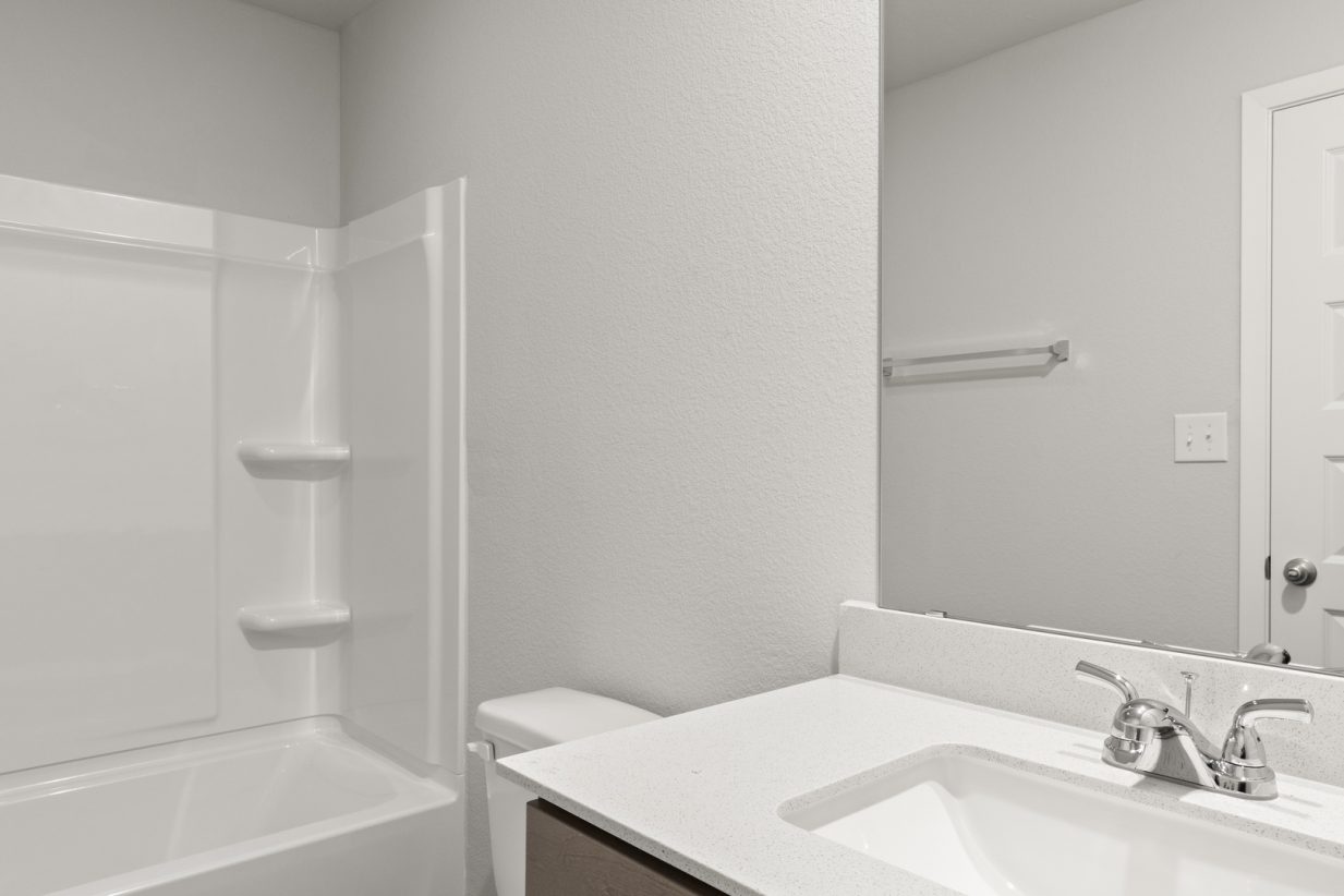 Image of a bathroom with light grey walls, a white vanity with a mirror and a white vinyl walk-in shower