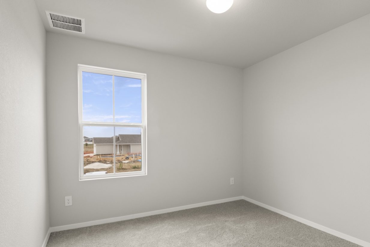Image of a bedroom with tan carpeting and light grey walls with a window