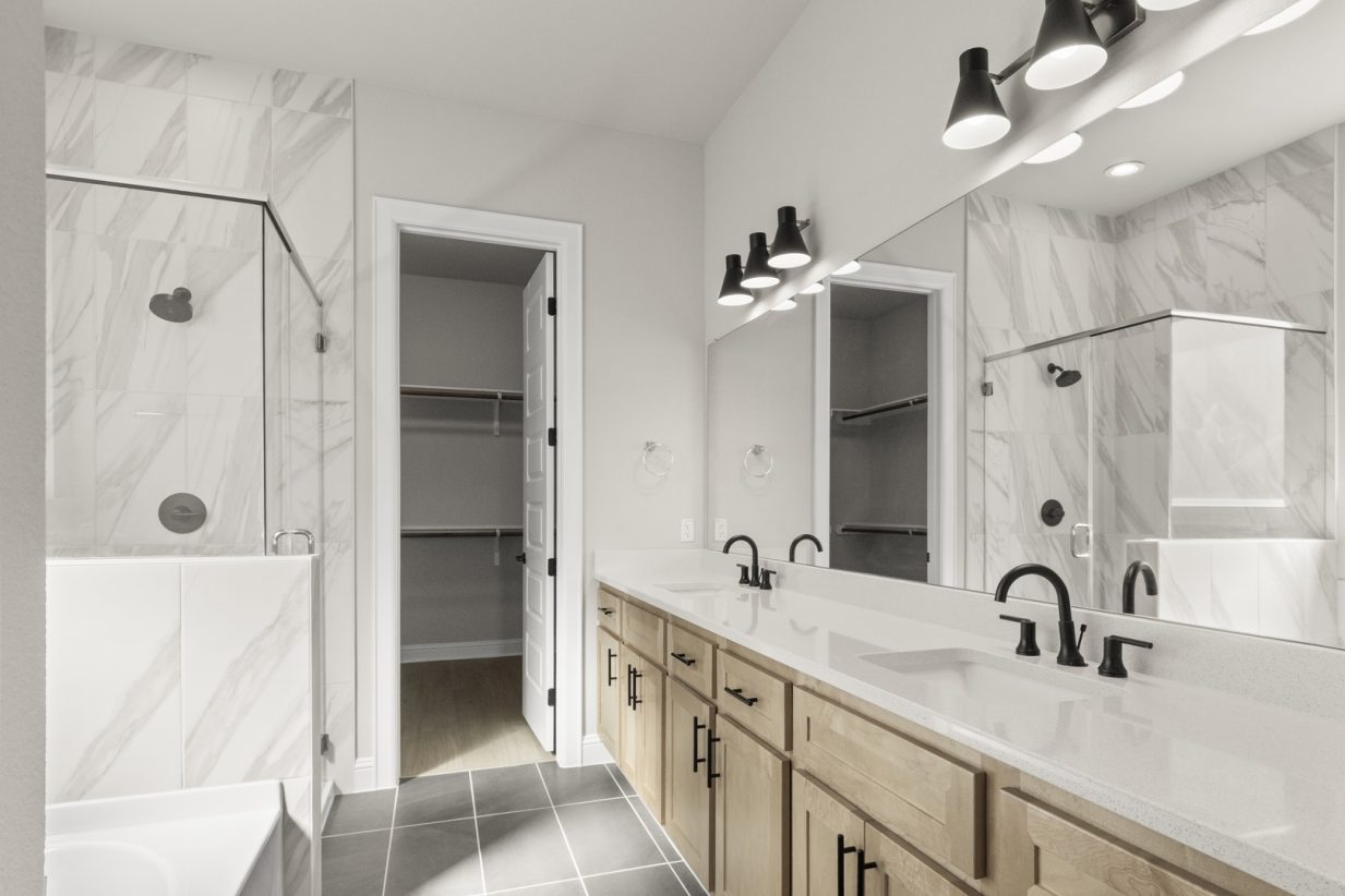 Image of a primary bathroom with marbled tile and a large vanity mirror with white countertops and brown cabinets, a walk-in shower, and a connected walk-in closet