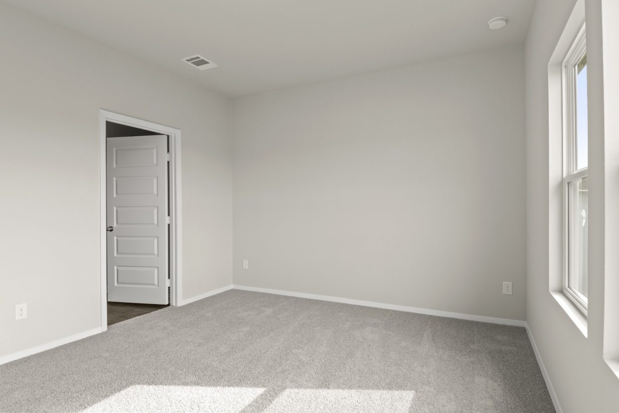 Image of primary bedroom with tan carpet and light grey walls with white door