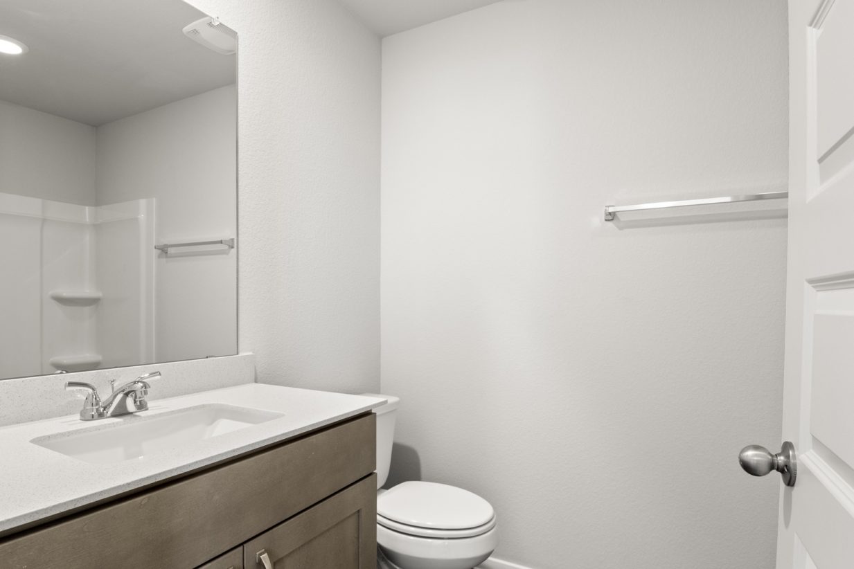 Image of a bathroom with light grey walls, a white vanity with brown cabinets and a mirror