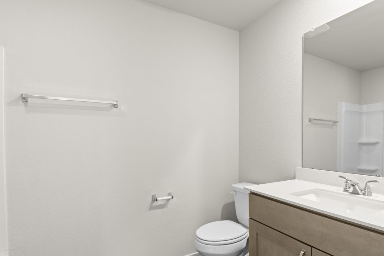 Image of a bathroom with light grey floors, brown cabinets, and a white vanity with a mirror