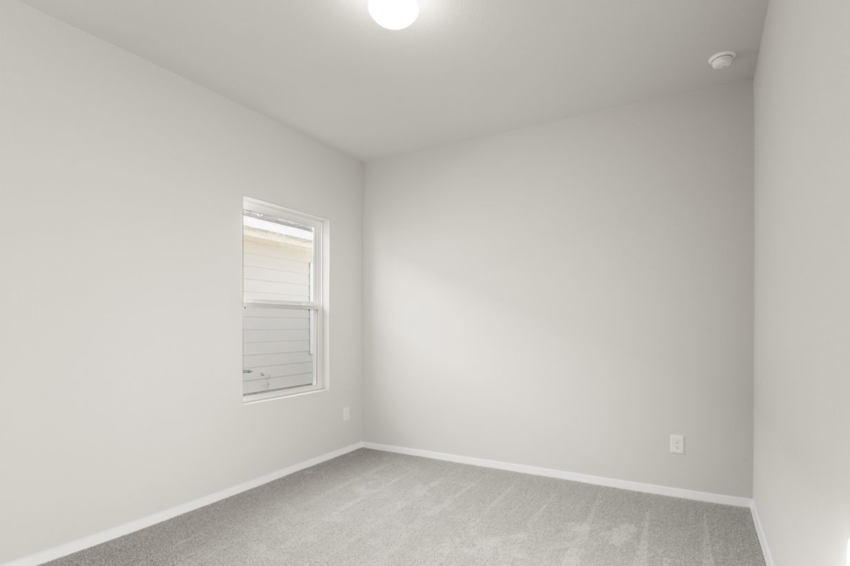 Image of a bedroom with light grey carpeting and painted walls with a window