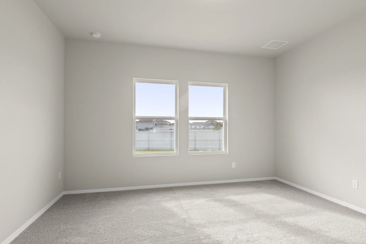 Image of primary bedroom with tan carpeting and light grey walls with two windows