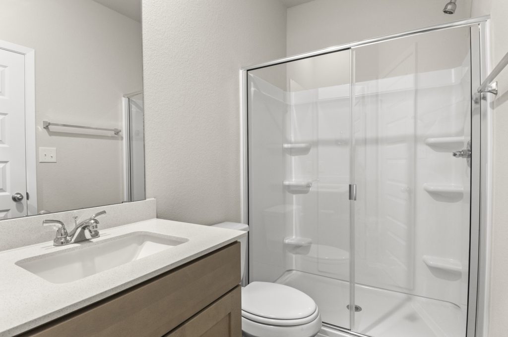 Image of primary bathroom with brown cabinets and a walk in shower with white vinyl