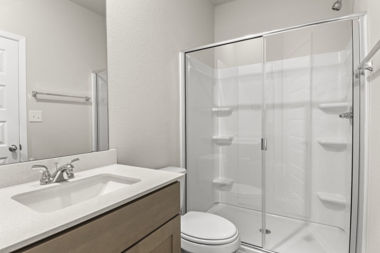 Image of primary bathroom with brown cabinets and a walk in shower with white vinyl