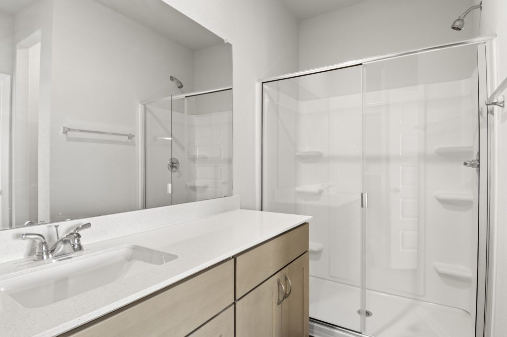 Image of primary bathroom with brown cabinets and a mirror with a white top vanity and a walk in shower