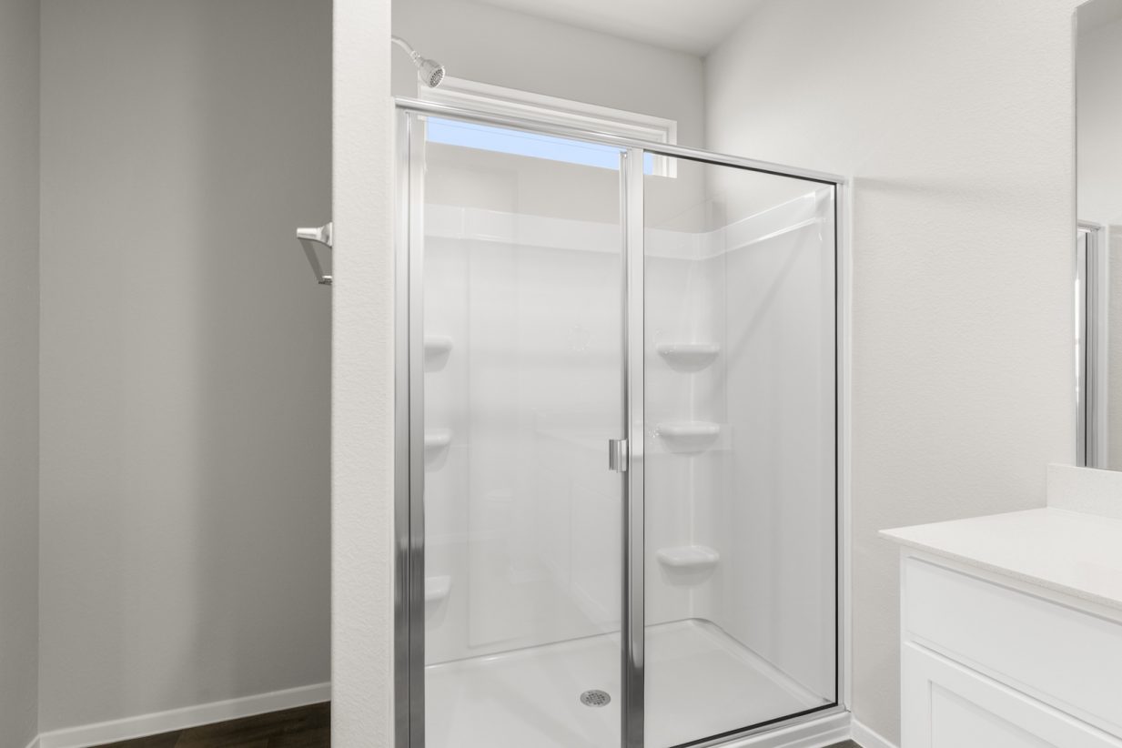 Image of a primary bathroom with cream walls, a white standing shower and a window above