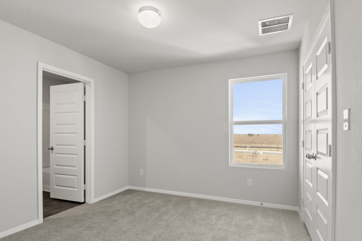 Image of a bedroom with light grey walls, tan carpeting, and a window