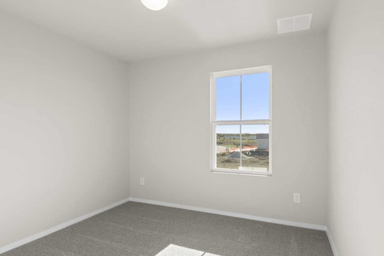 Image of a bedroom with tan carpeting, light grey walls and a window