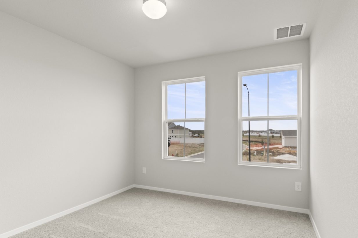 Image of a bedroom with tan carpeting and light grey walls with two windows