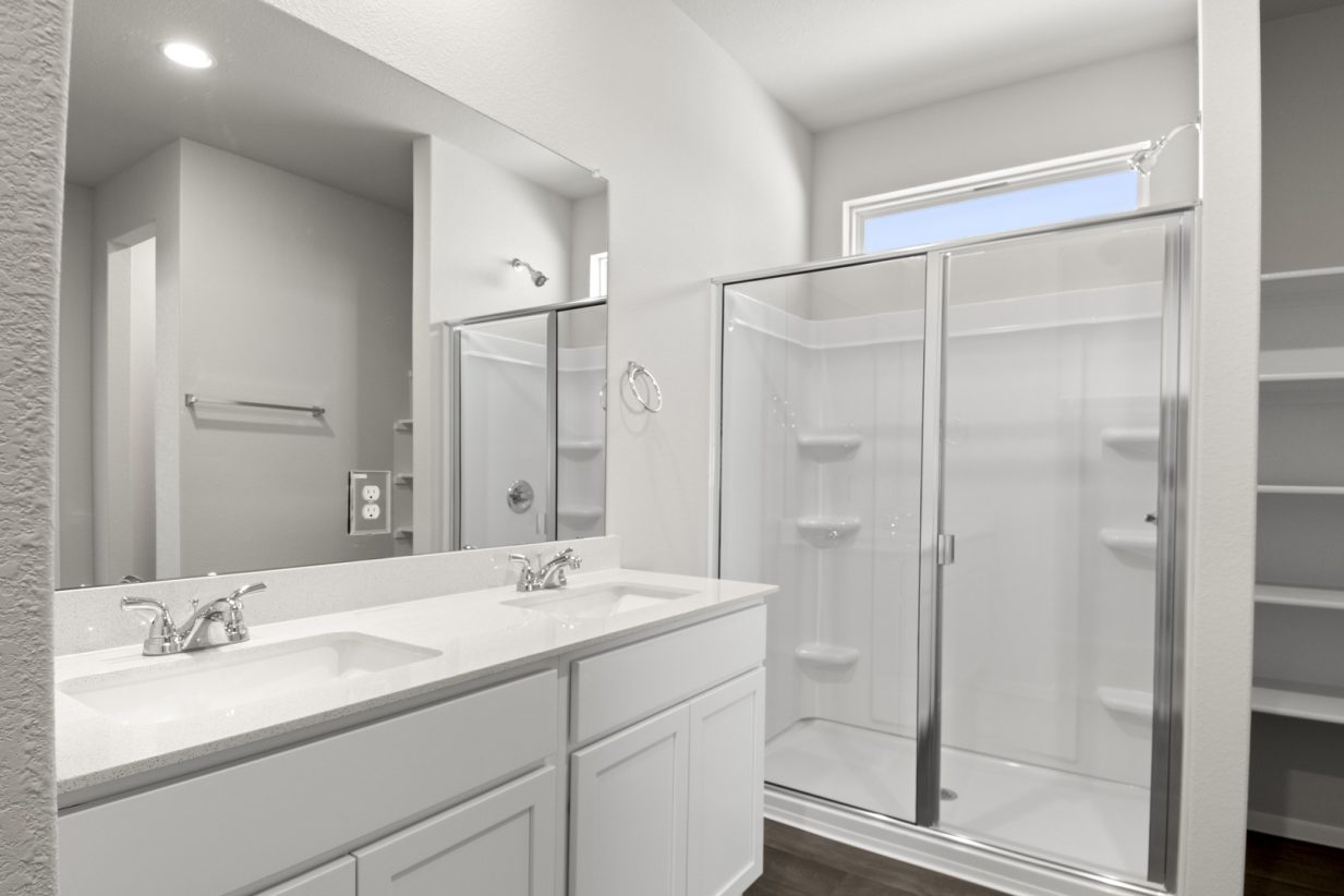 Image of a primary bathroom with which cabinets and jack and jill vanity, a large mirror, and a walk-in shower, and a window above the shower