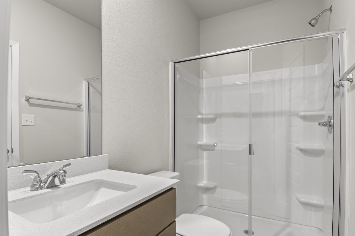 Image of a primary bathroom with a white vanity, brown cabinets, and a walk-in shower