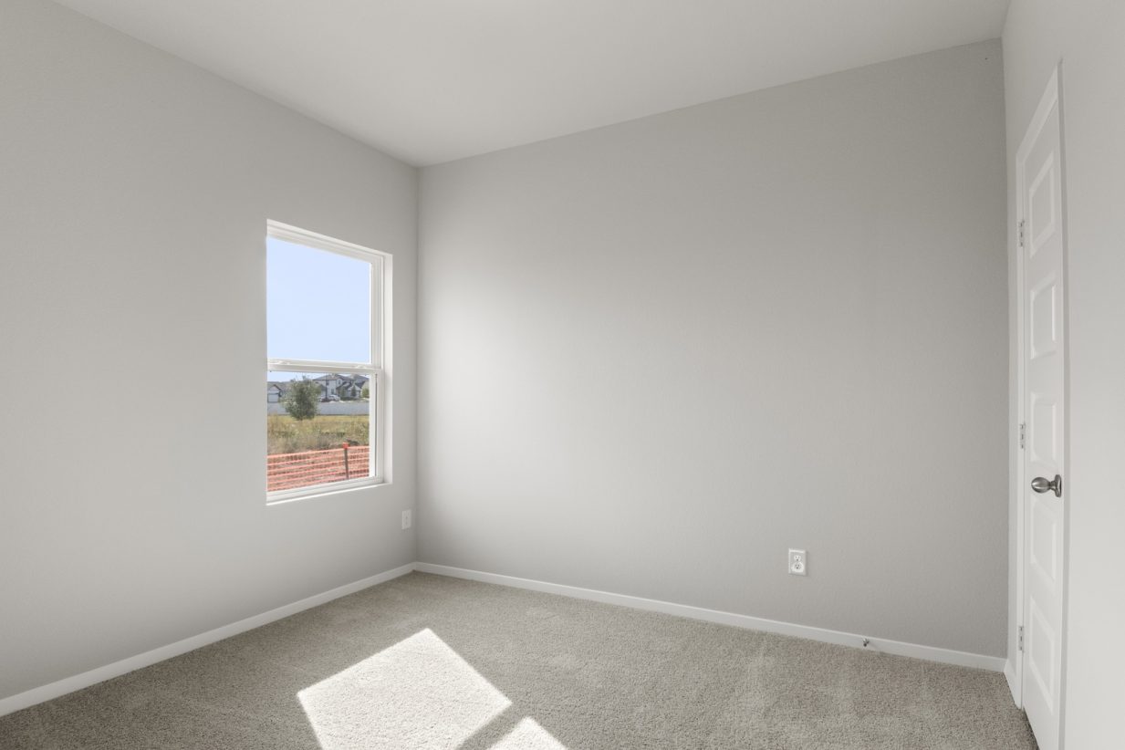 Image of bedroom with tan carpet and light grey walls with a window