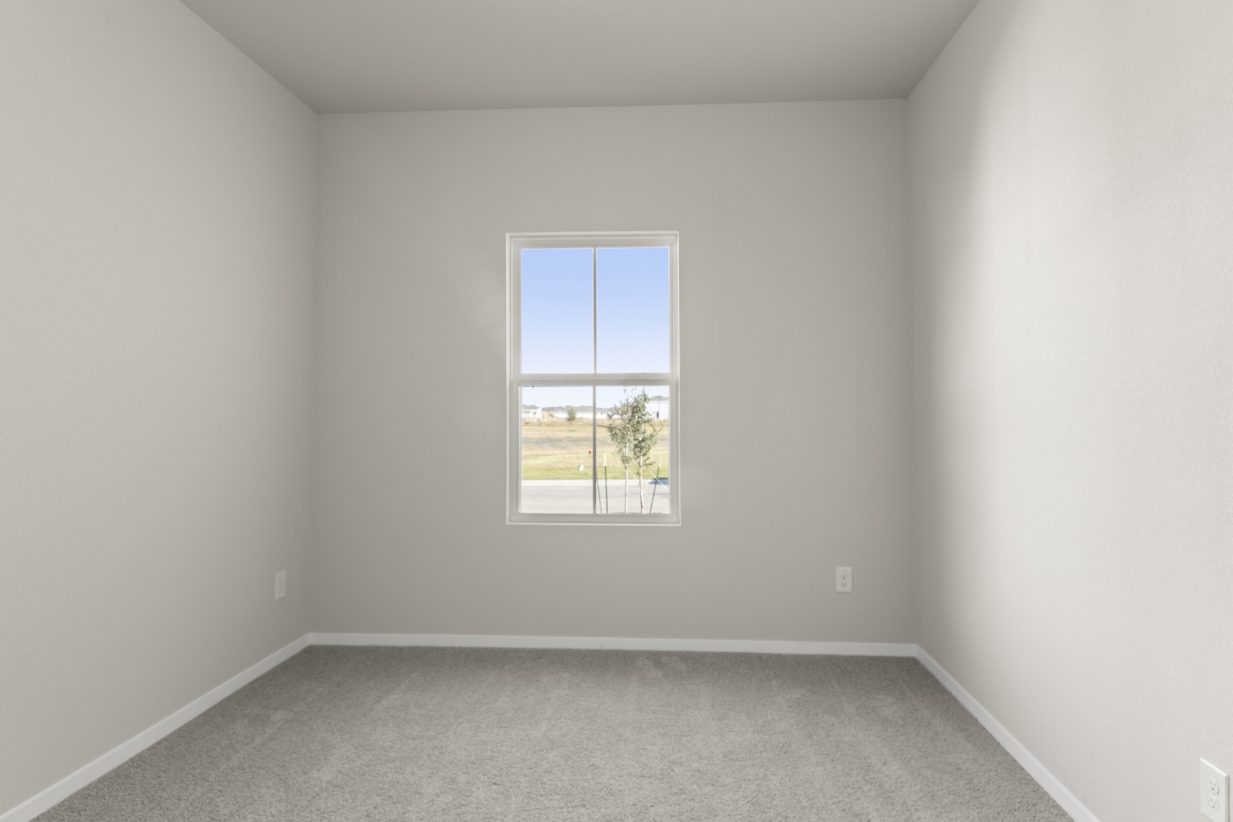 Image of a bedroom with light grey carpeting and painted walls with a window