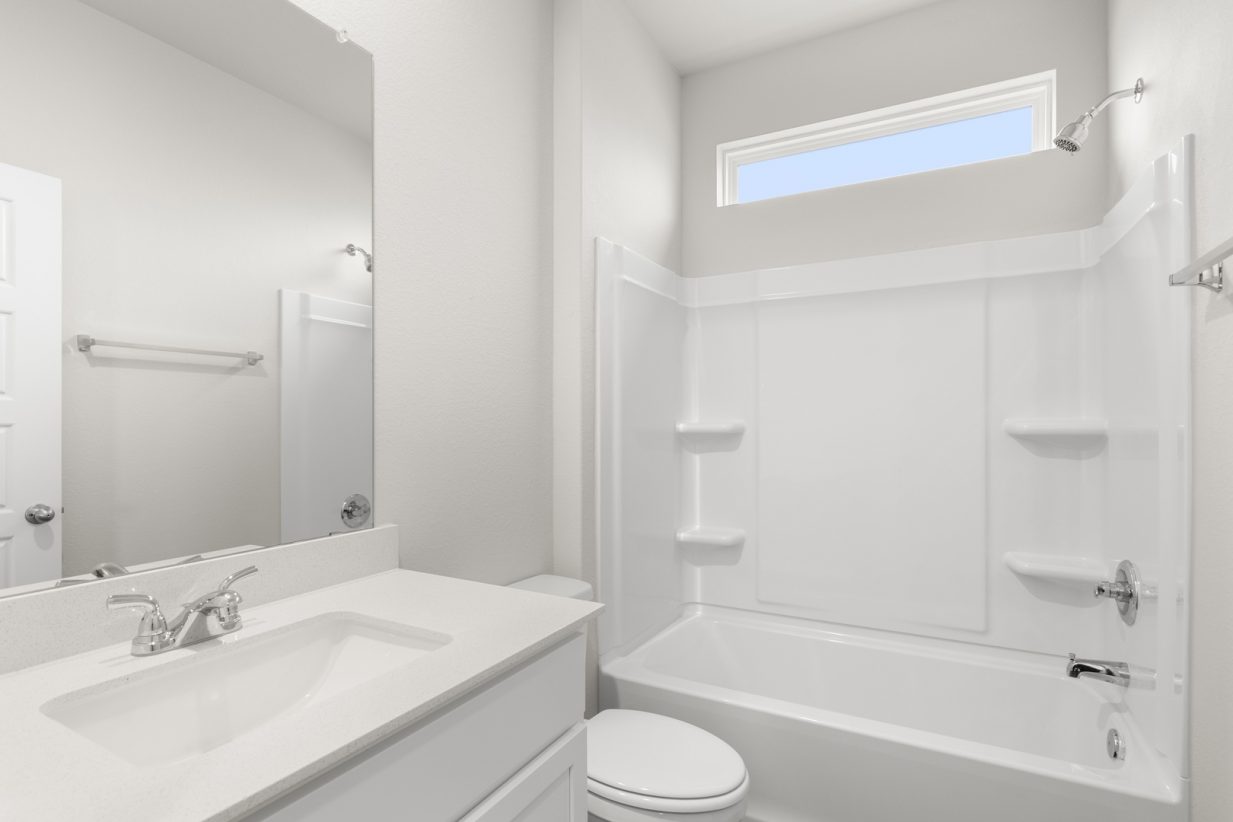 Image of a bathroom with a white vanity and cabinets, mirror, and a white shower ILO tub with a window above