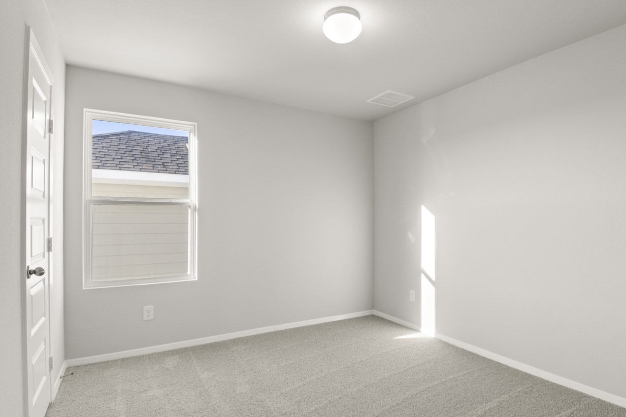 Image of a bedroom with tan carpeting and light grey painted walls with a window