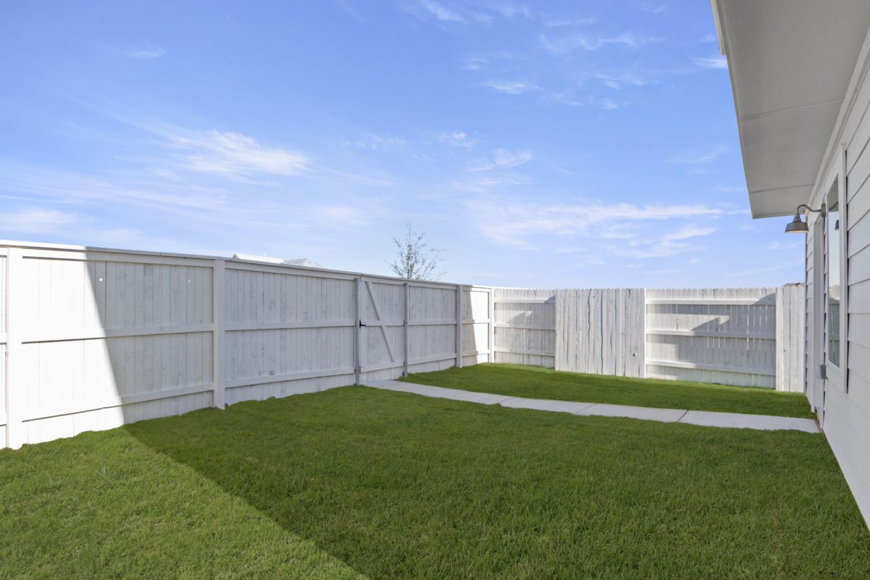 Image of a cottage home backyard with green grass, a white wooden fence, and a blue sky in the background