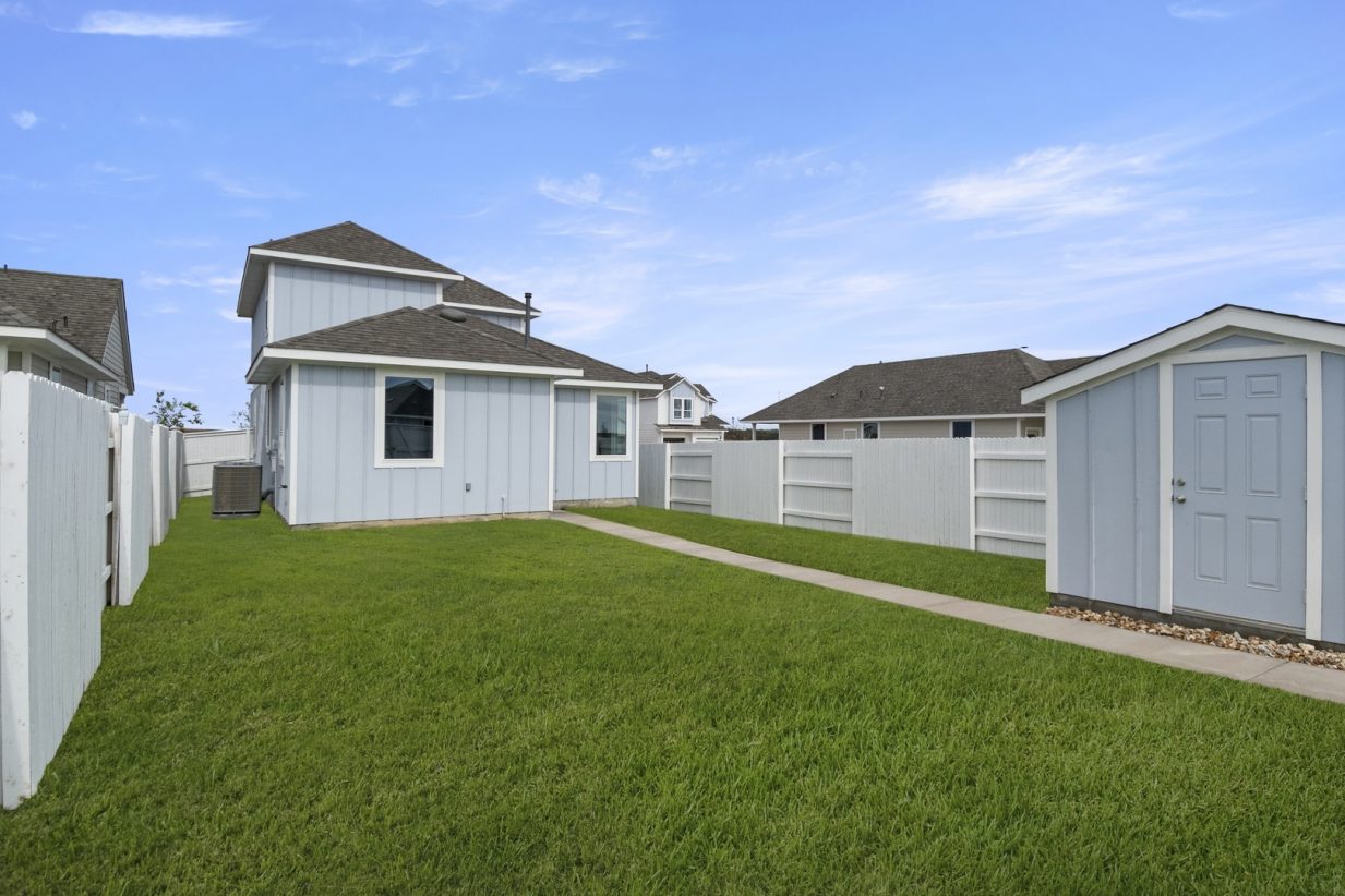 Image of the back exterior of a two story grey home with a pathway and a green grass backyard