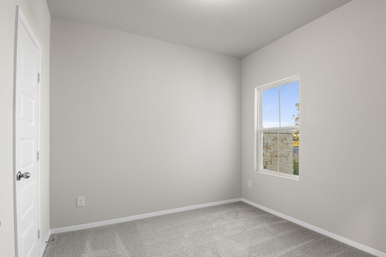 Image of a bedroom with light grey carpeting and painted walls with a window