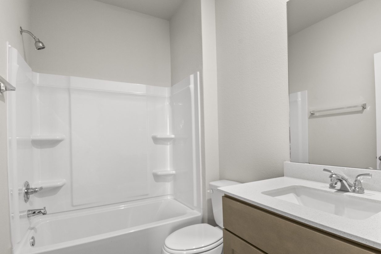Image of a bathroom with white vinyl shower and tub, white vanity, and brown cabinetry