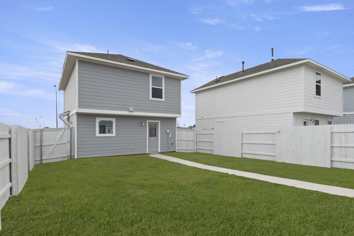 Image of the back exterior of a grey two story cottage home with a large green grass backyard and a white fence