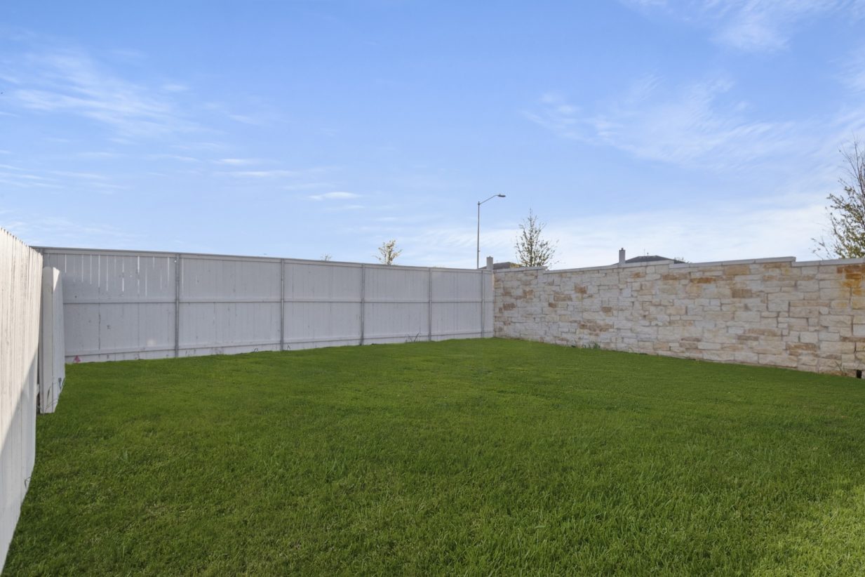 Image of a backyard with green grass and a wooden white fence connecting to beige stone fence