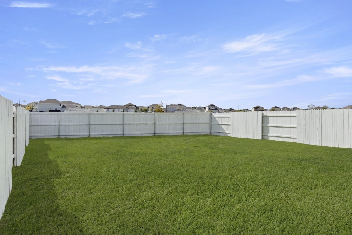 Image of backyard with green grass and a white fence