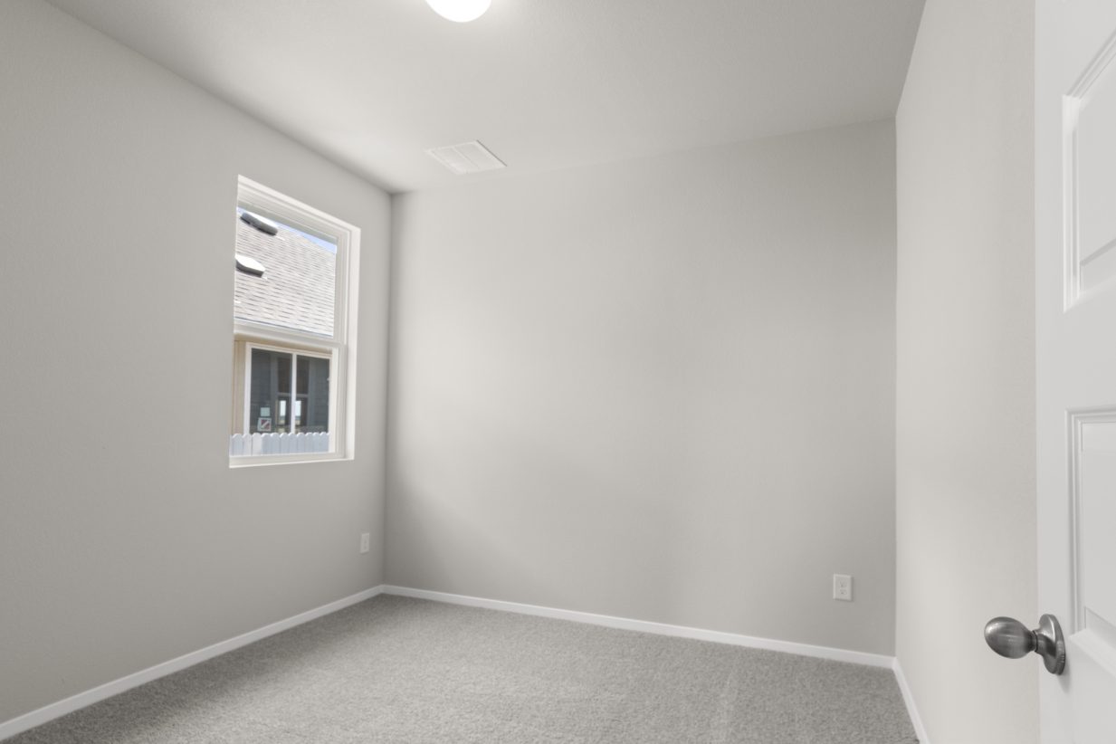 Image of a bedroom with light grey walls and carpeting and a window in the corner
