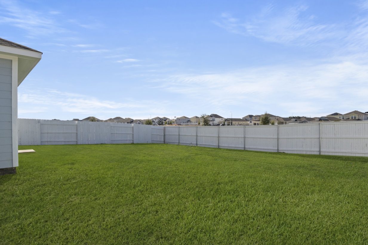Image of a green grass backyard with a white fence and blue sky