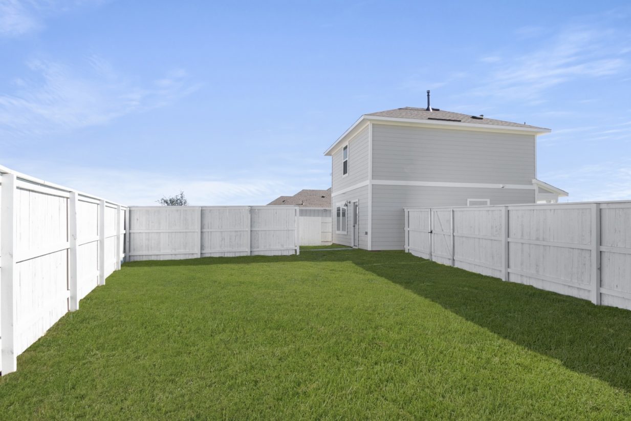 Image of a cottage home backyard with green grass, a white fence and a blue sky in the background