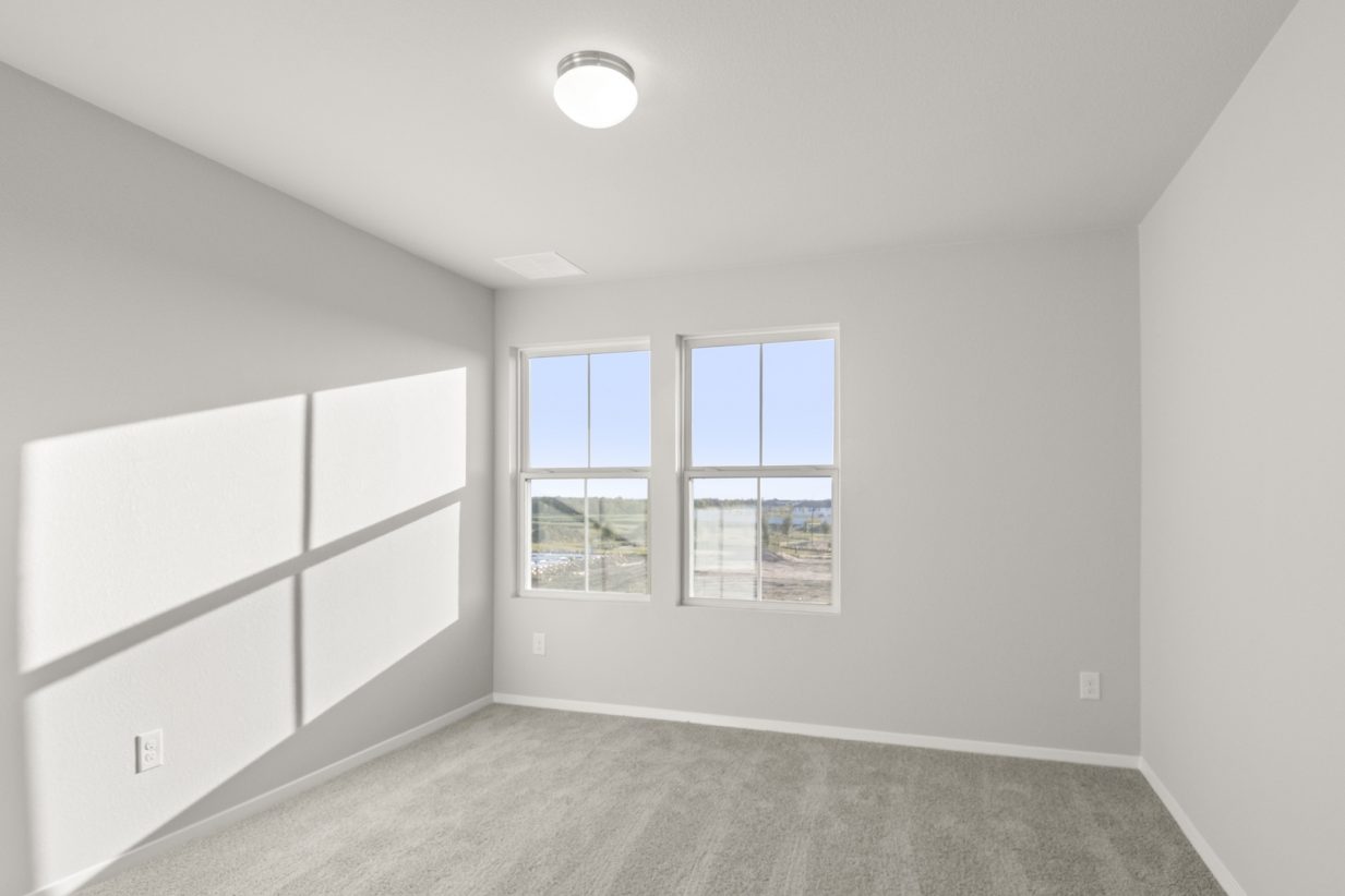 Image of a bedroom with tan carpeting and light grey painted walls with two windows
