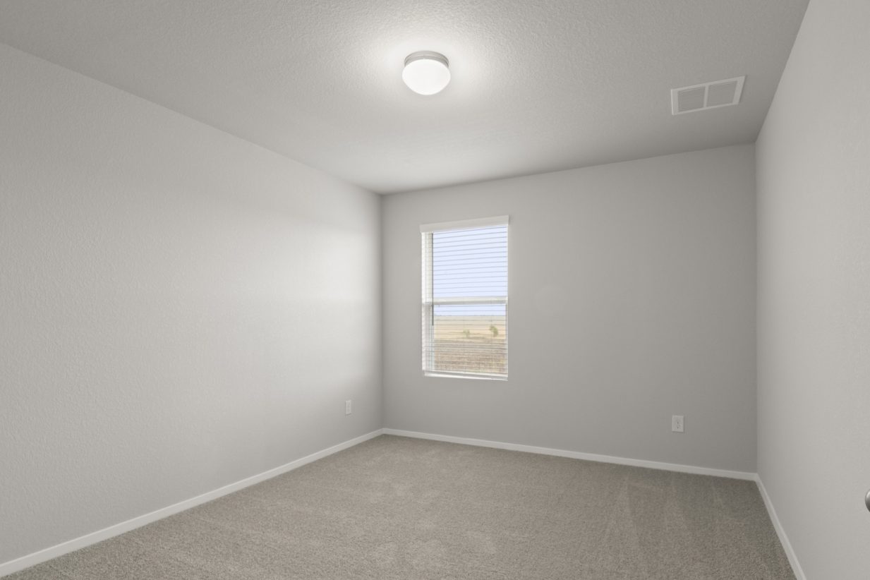 Image of a bedroom with tan carpeting and light grey walls with a window