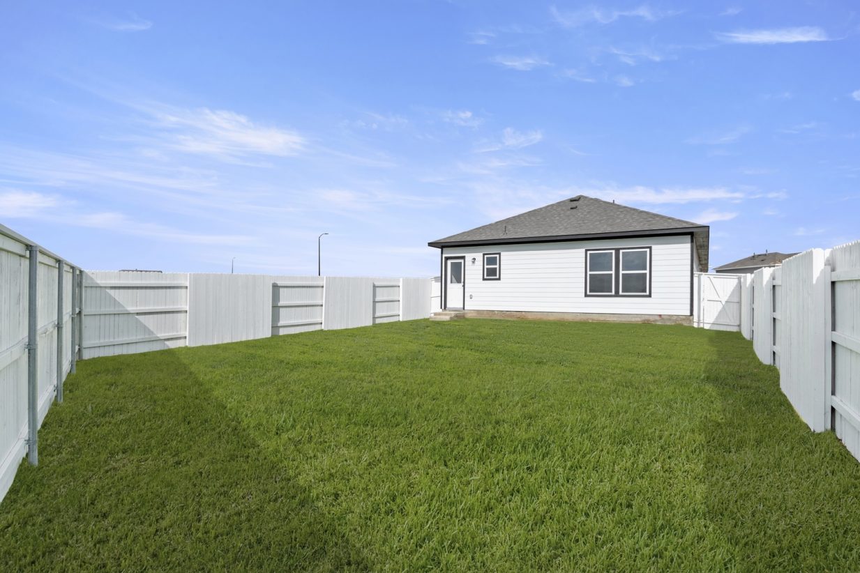 Image of a white house and backyard with green grass and a white fence