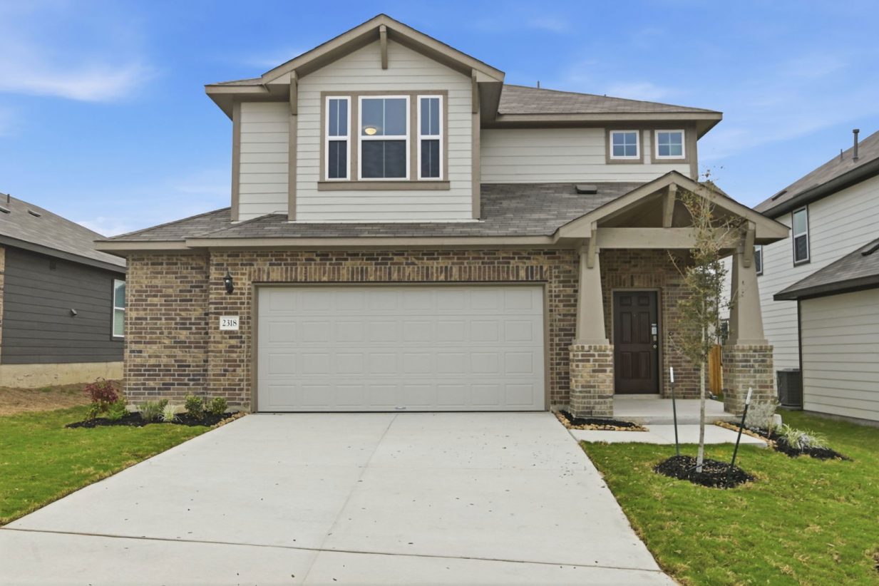 Image of a two story home with light brown paint, brick masonry, a cream garage and a cement driveway