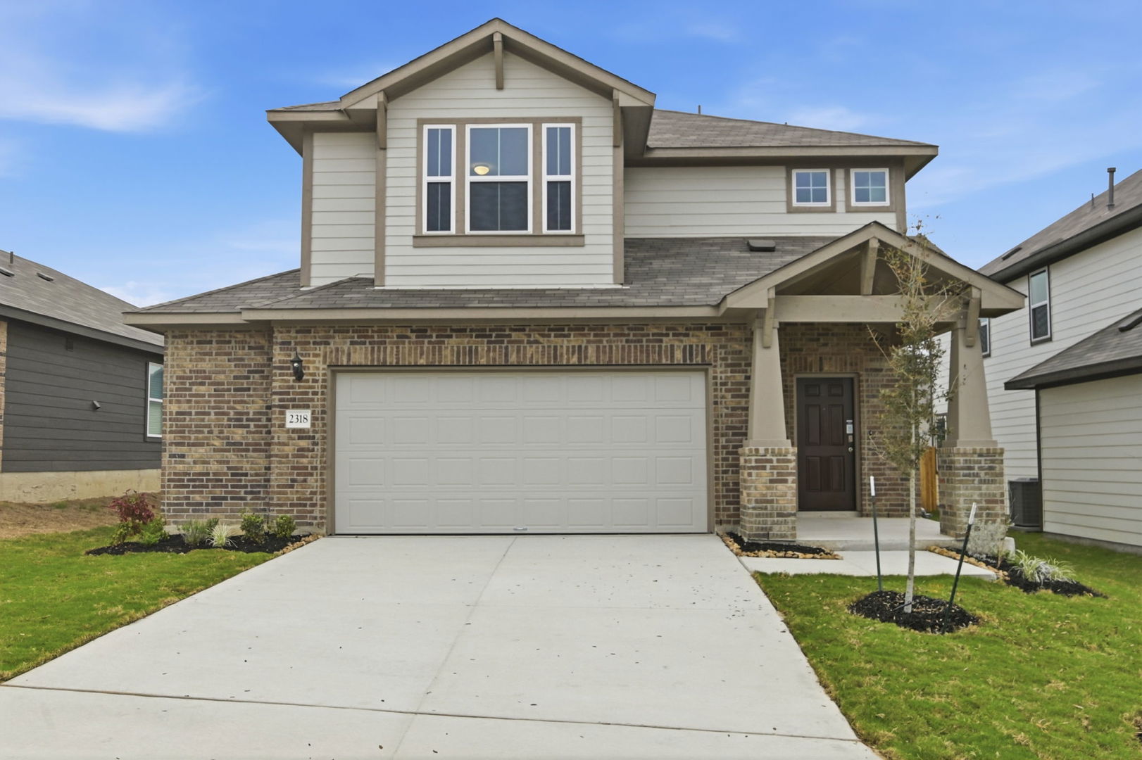 Image of a two story home with light brown paint, brick masonry, a cream garage and a cement driveway