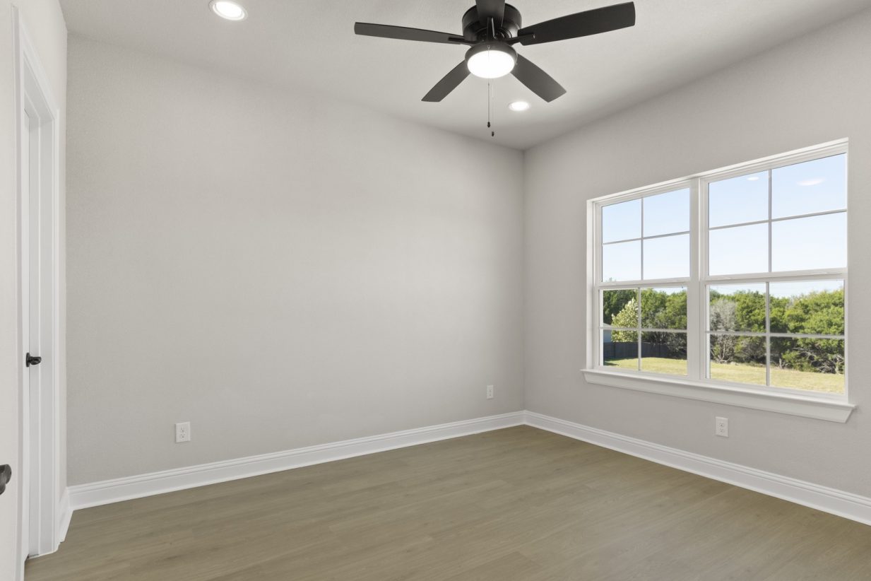 Image of a two story home bedroom with light wooden flooring and light grey painted walls with a ceiling fan and two windows