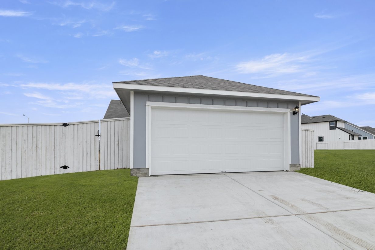 Image of an ally access garage with a white door, a cement driveway and a white wooden fence
