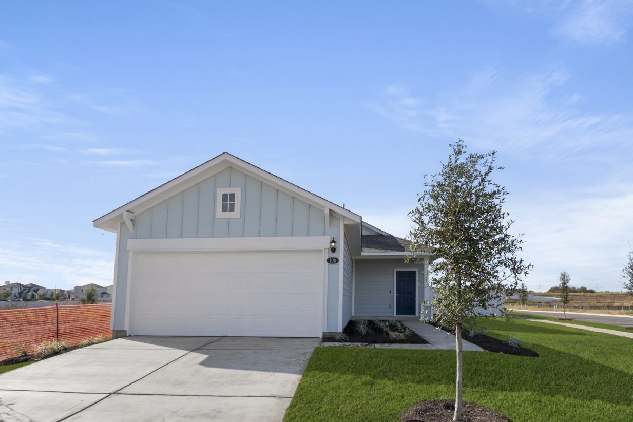 Image of a blue one story home with a dark blue door and a two car garage with a cement driveway with green grass and a blue sky