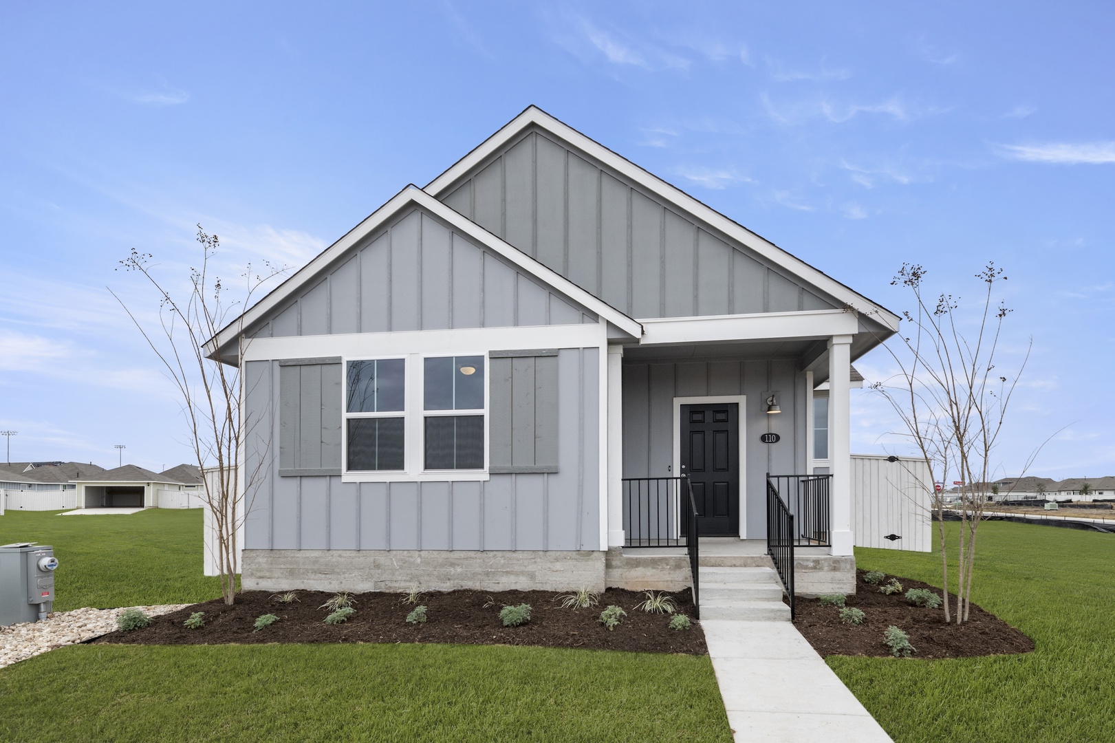 Image of a grey one story home front exterior with white trim, grey shutters, a black front door, green grass and a blue sky in the background