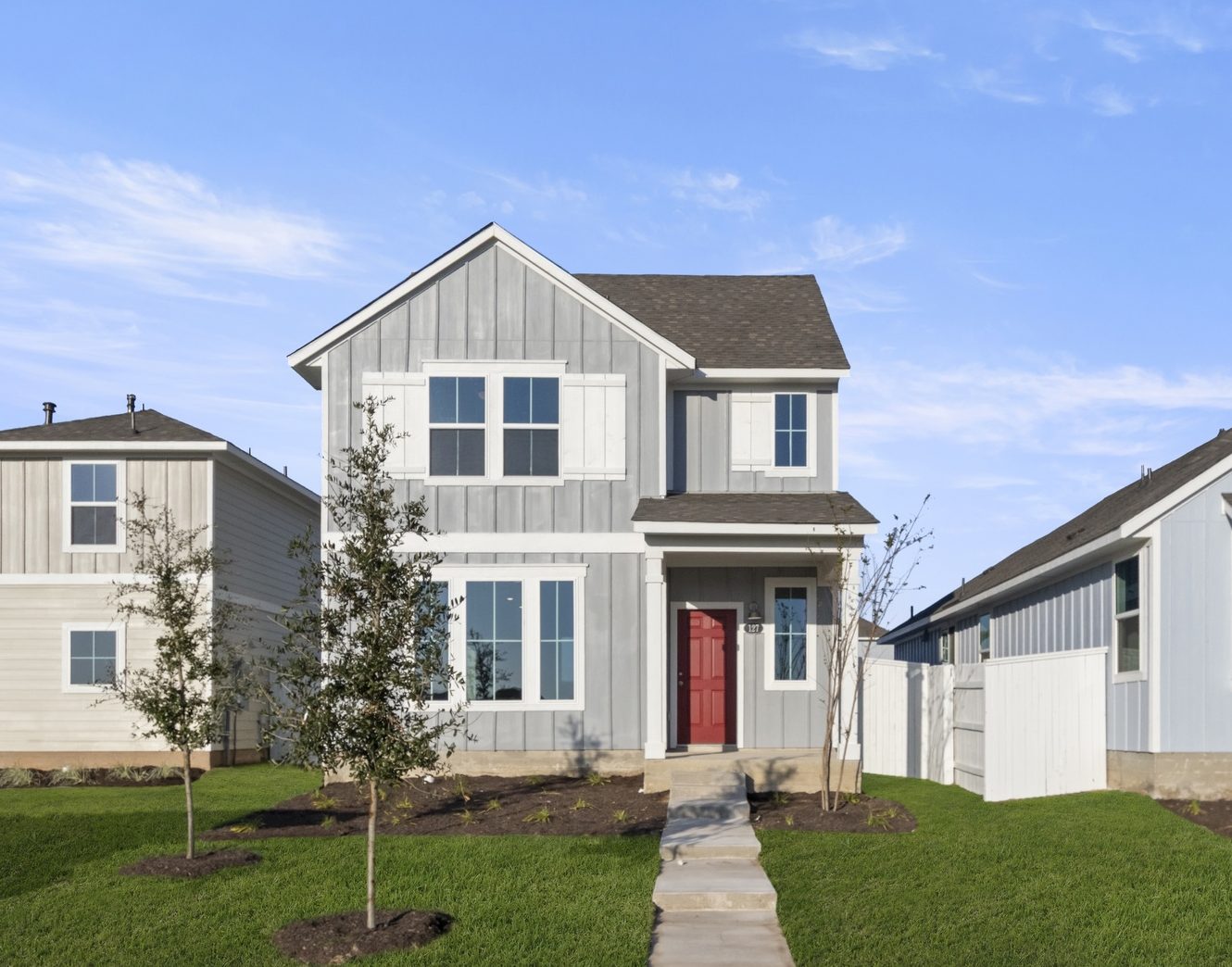 Image of the front exterior of a grey two story house with a red front door and white trim and shutters with green grass and a blue sky