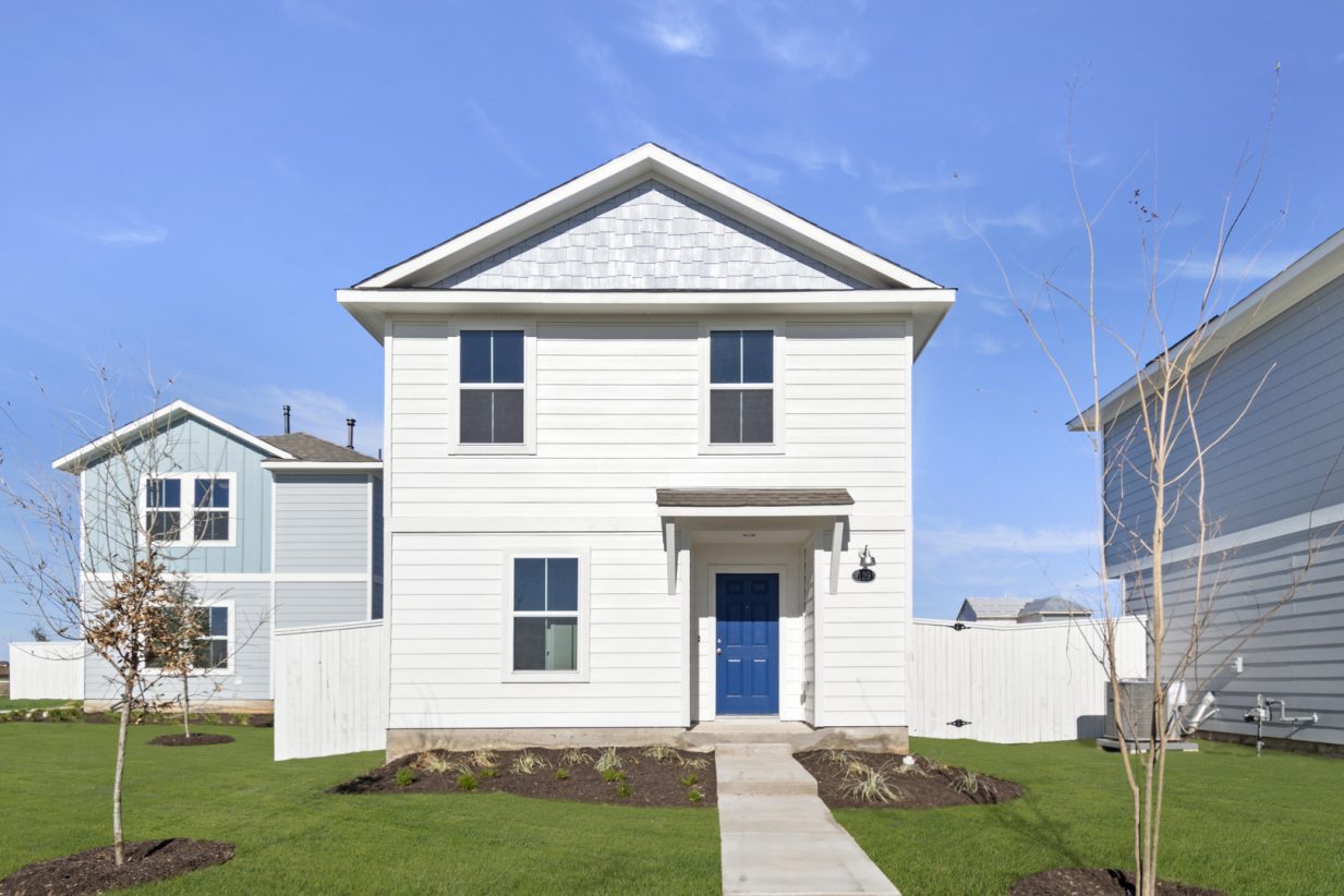 Image of a two story white cottage home with windows, a blue front door, a cement pathway, green grass and a blue sky in the background