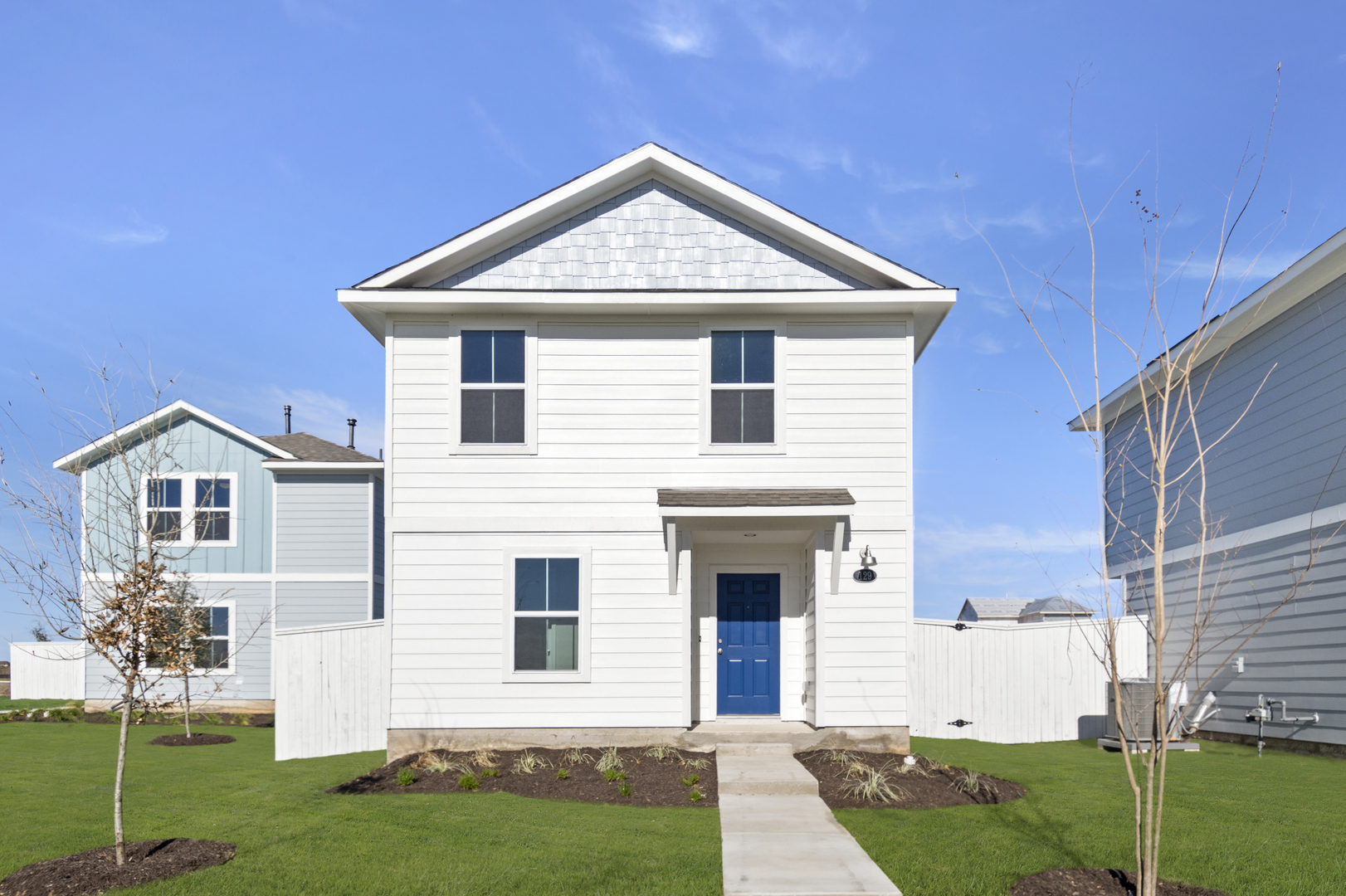 Image of a two story white cottage home with windows, a blue front door, a cement pathway, green grass and a blue sky in the background