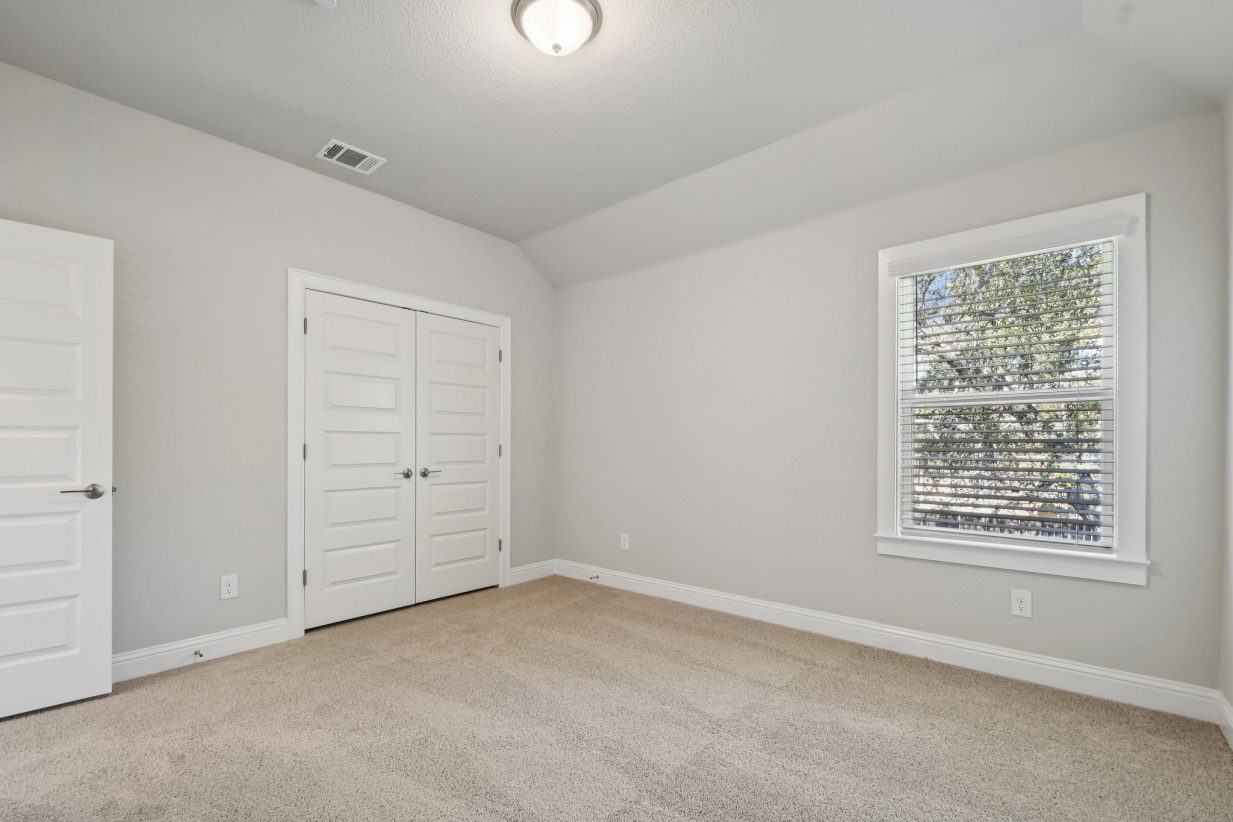 Image of a bedroom with light grey walls, tan carpeting, a window, and white trim