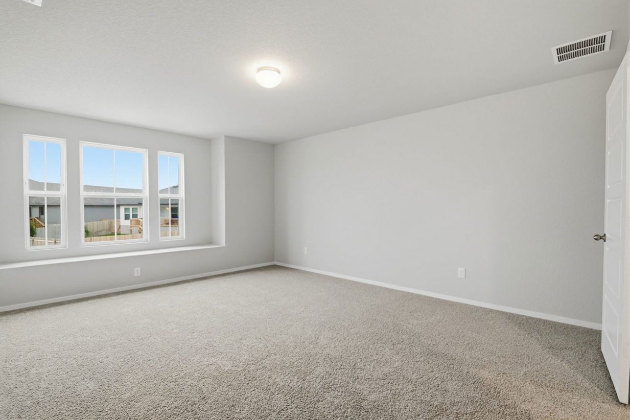 Image of a primary bedroom with light grey walls, tan carpeting, windows and a large window seal