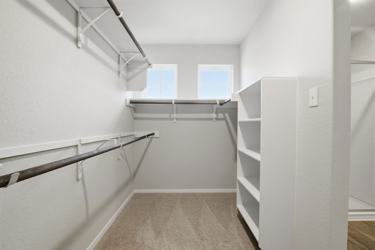 Image of a large walk-in primary closet with light grey walls, shelfs, and windows