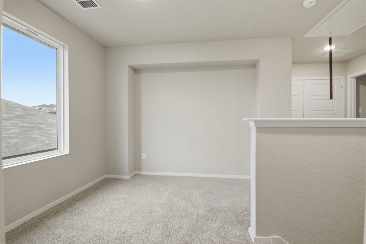 Image of a upstairs loft with light grey walls, a large window and tan carpeting