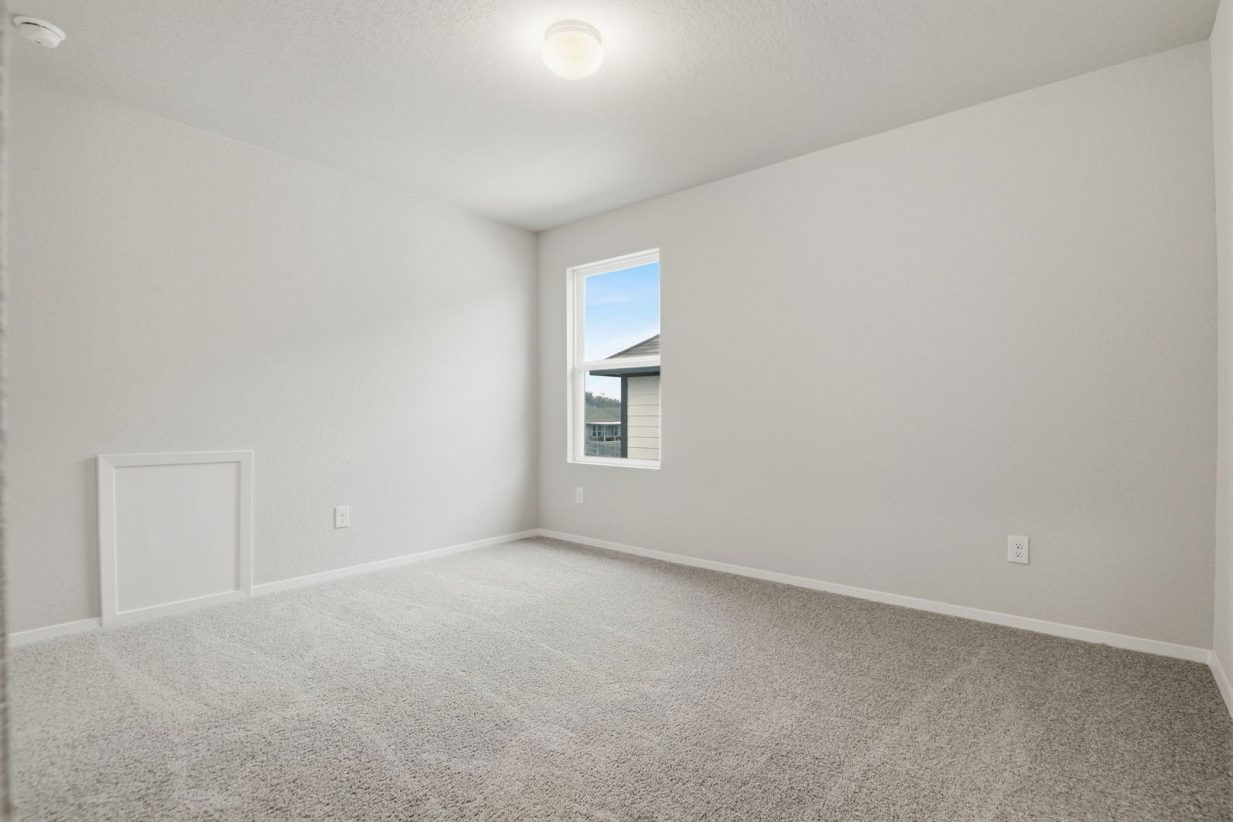 Image of a bedroom with light grey walls, tan carpeting, a window and white trim